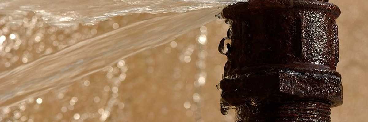 A rusty pipe with a leak spewing water.