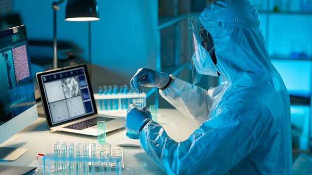 A scientist in a hazmat suit testing liquids in beakers