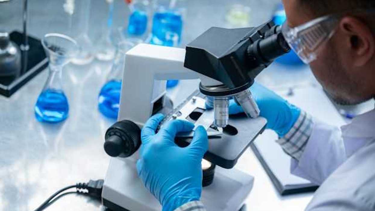 A scientist wearing blue gloves looks through a microscope