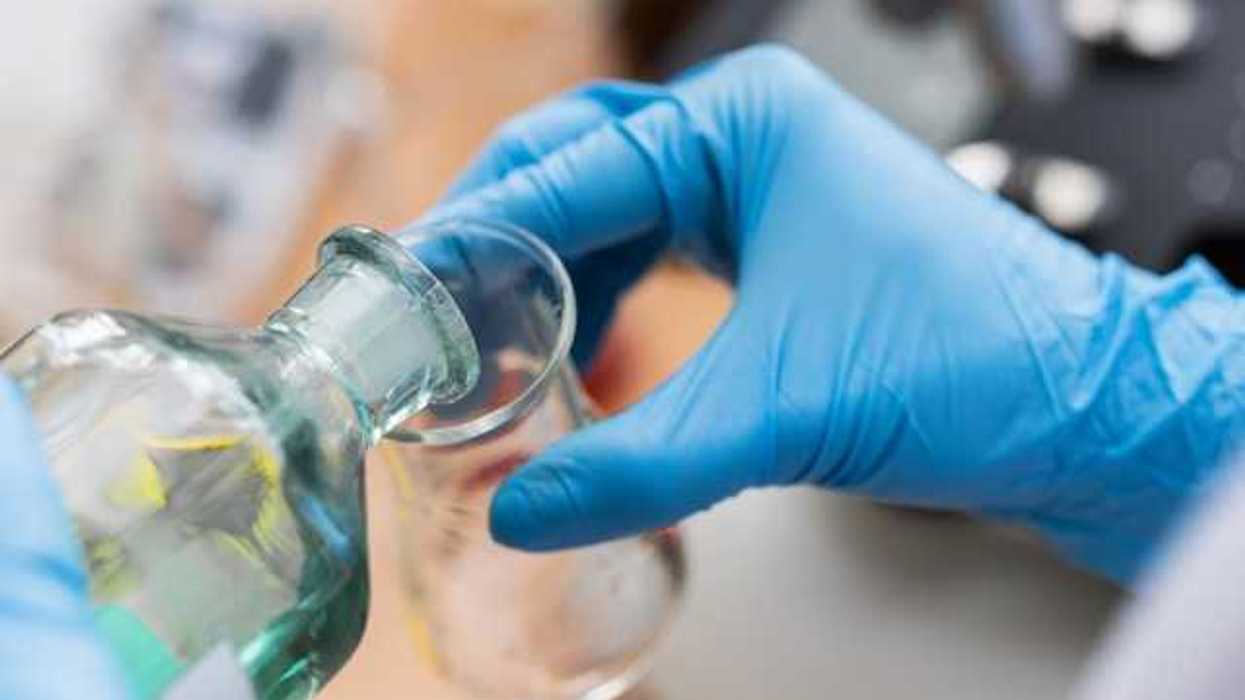 A scientist wearing blue lab gloves pouring liquid into a beaker