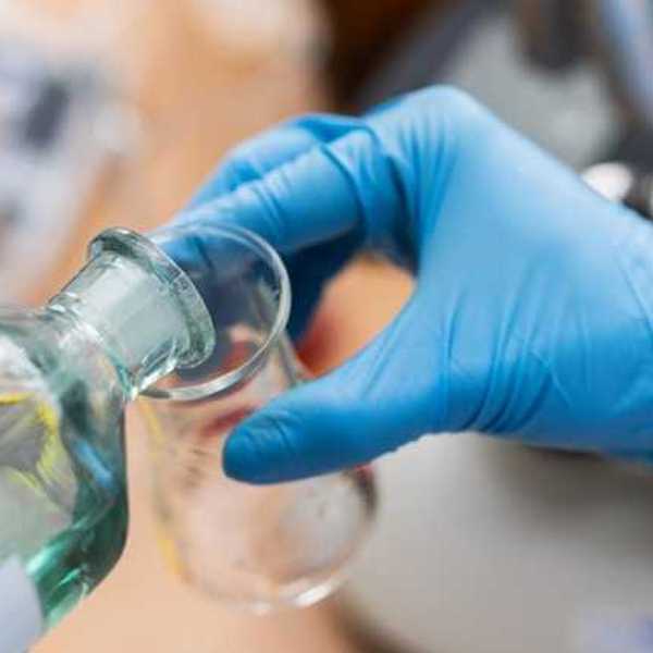 A scientist wearing blue lab gloves pouring liquid into a beaker