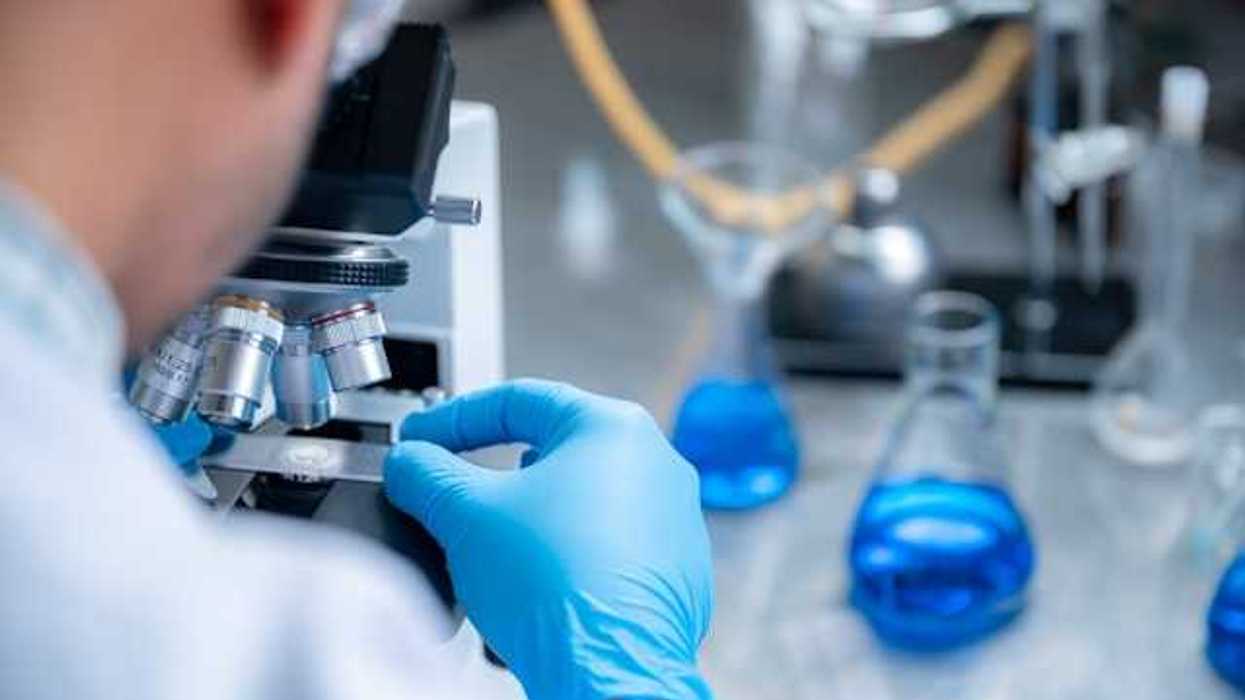 A scientist wearing blue plastic gloves looking through a microscope