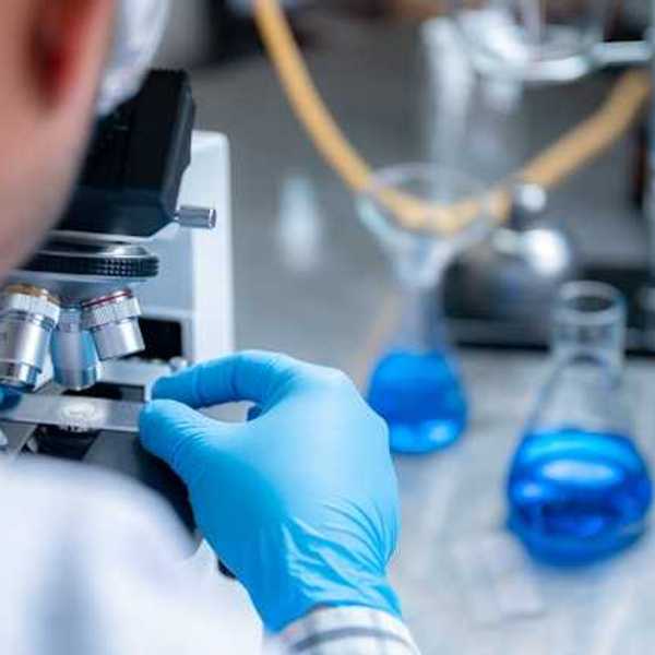 A scientist wearing blue plastic gloves looking through a microscope
