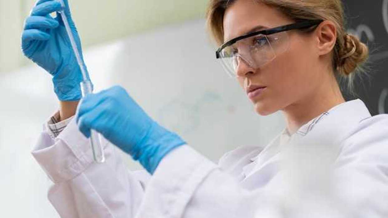 A scientist wearing safety glasses and looking at a test tube