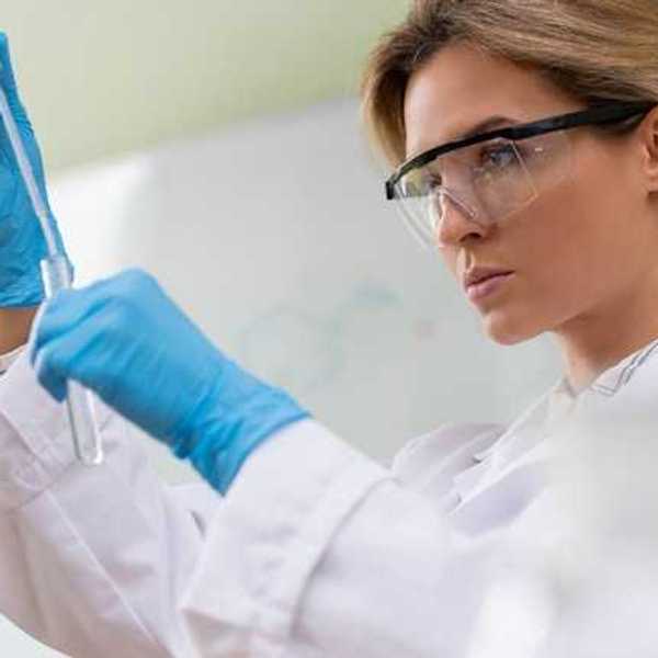 A scientist wearing safety glasses and looking at a test tube