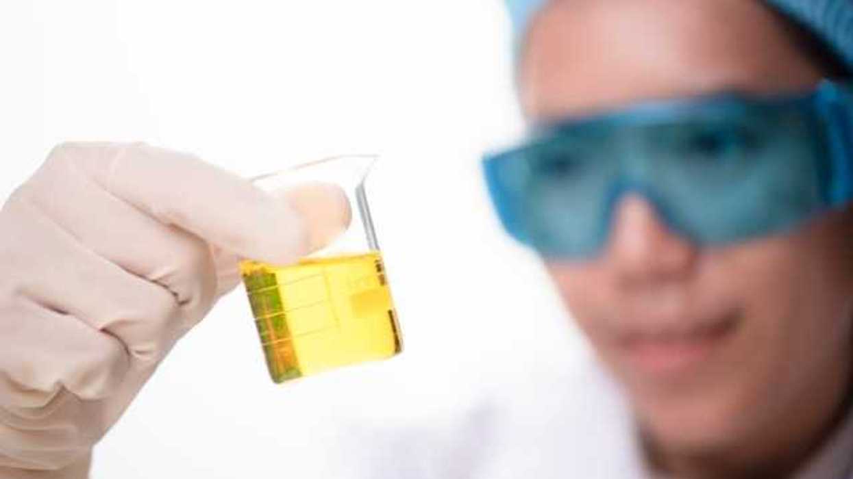 A scientist with eye protection goggles looking at a jar with yellow liquid