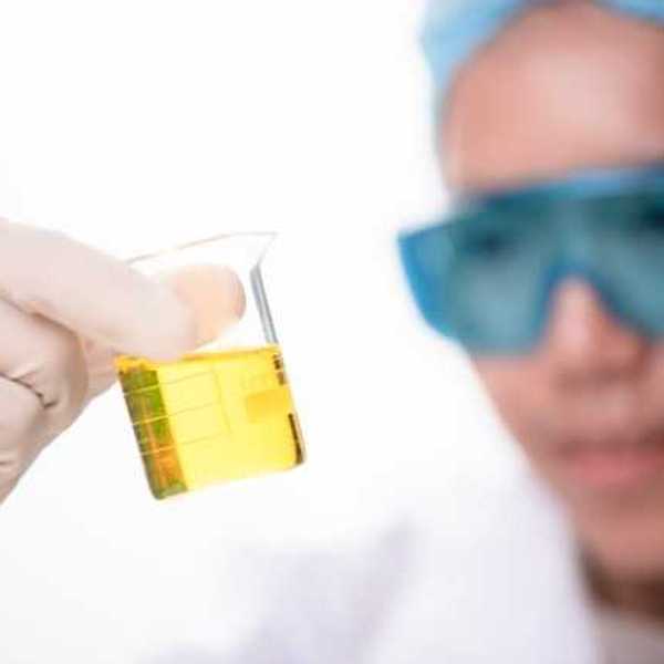 A scientist with eye protection goggles looking at a jar with yellow liquid