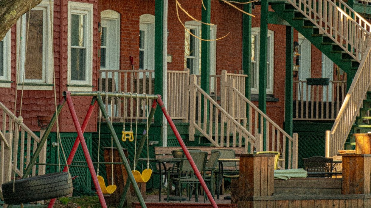A series of row houses with stairs leading to porches and a swing set in the front yard.