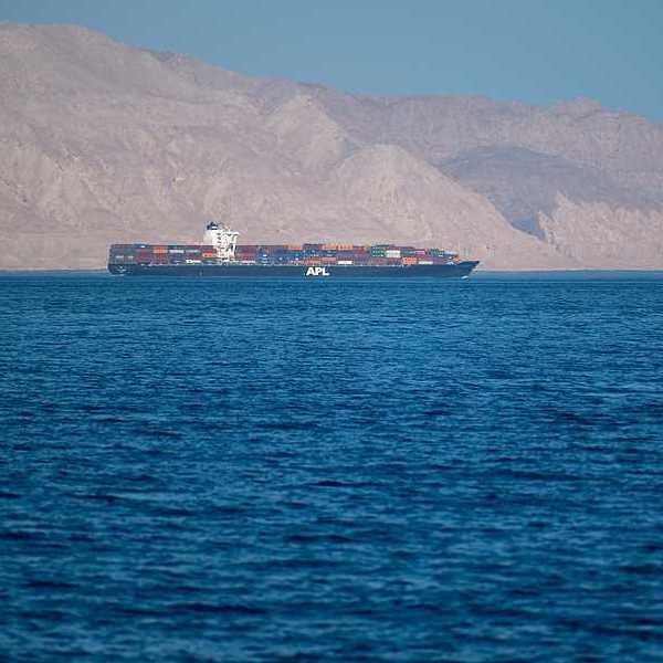 A ship sailing through the Strait of Hormuz with dry mountains in the background