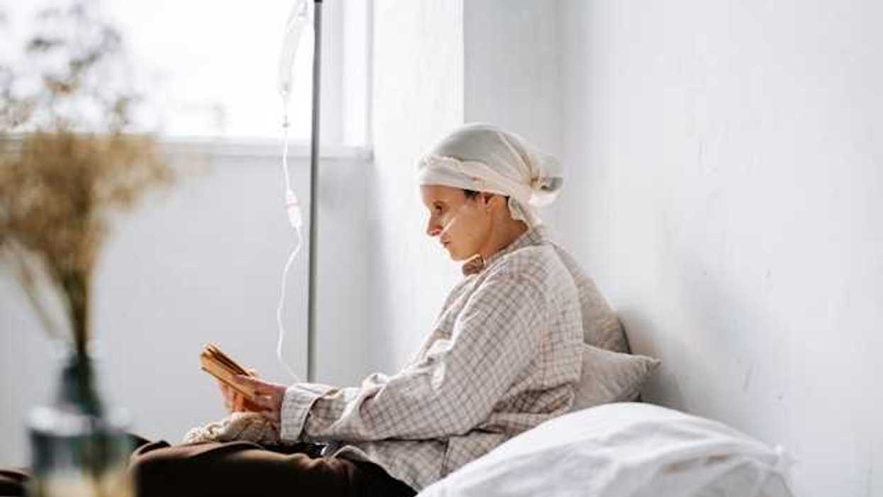 A side view of a cancer patient hooked up to an IV reading a book