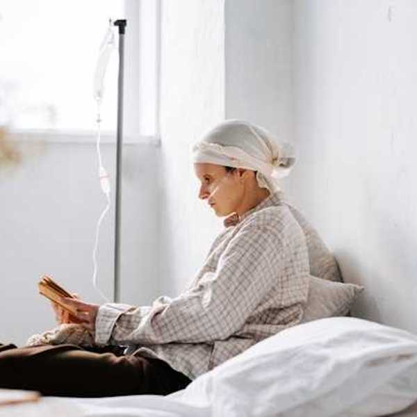 A side view of a cancer patient hooked up to an IV reading a book