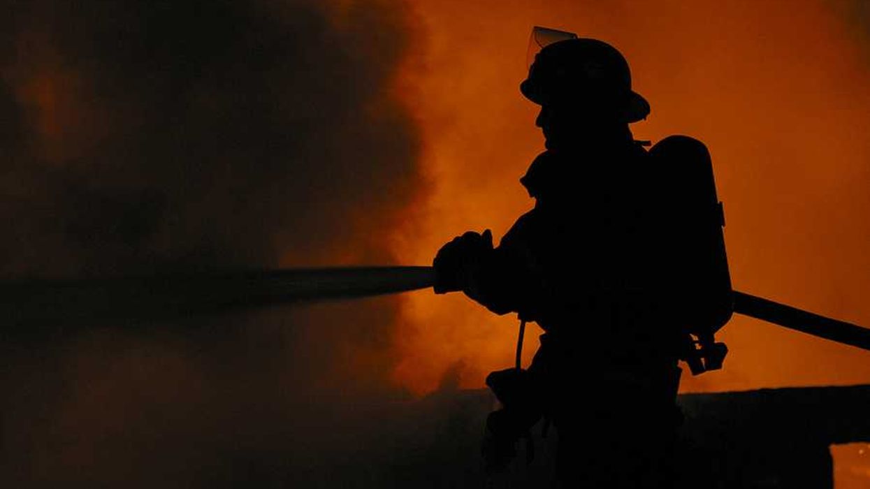 A silhouette of a firefighter spraying water on a fire with billowing smoke