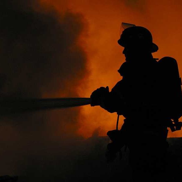 A silhouette of a firefighter spraying water on a fire with billowing smoke