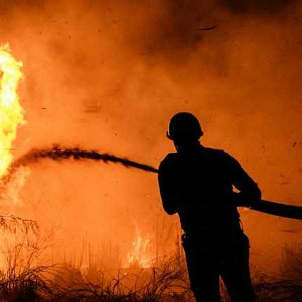 A silhouette of a firefighter spraying water on a wildfire
