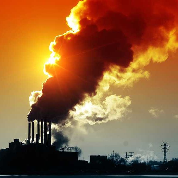 A silhouette of a power plant with billowing smoke and the sun in the background