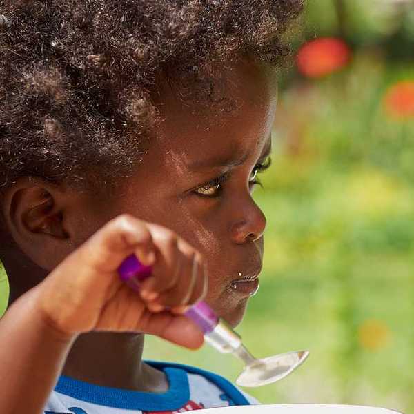 A small black child eating with a spoon