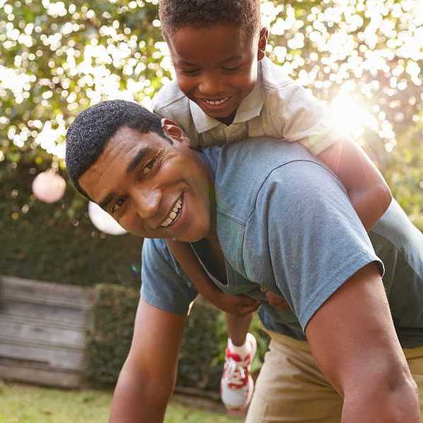 A small Black child riding on his father's back in a beautiful garden setting