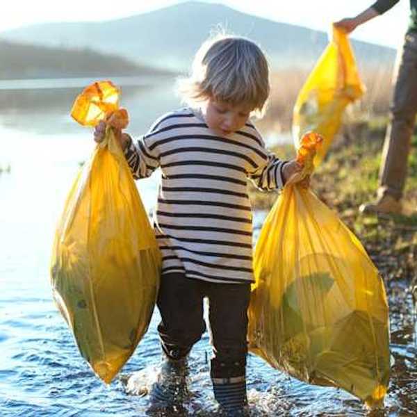 A small boy carrying two plastic bags of trash while walking in a lake