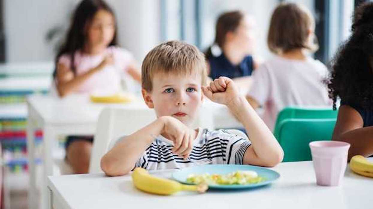 A small boy sitting at a desk with a banana and a plate of food in front of him
