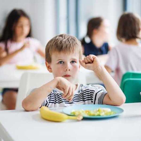 A small boy sitting at a desk with a banana and a plate of food in front of him