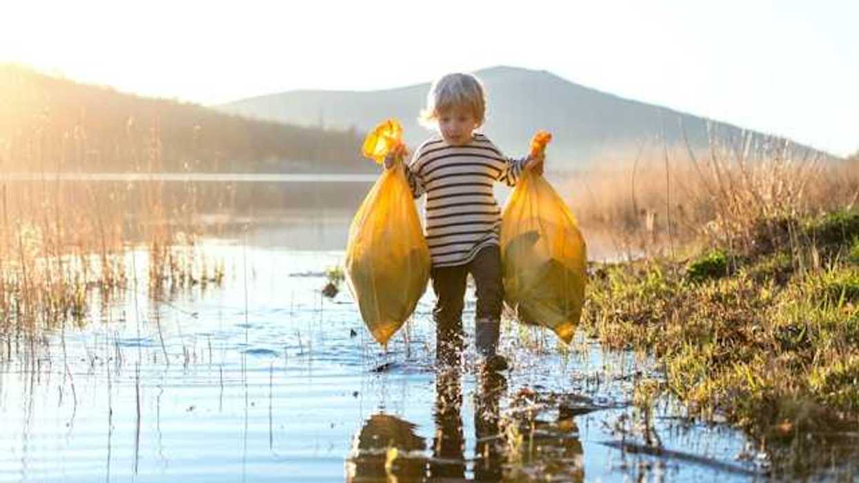 A small boy walking through a shallow lake with two bags of trash