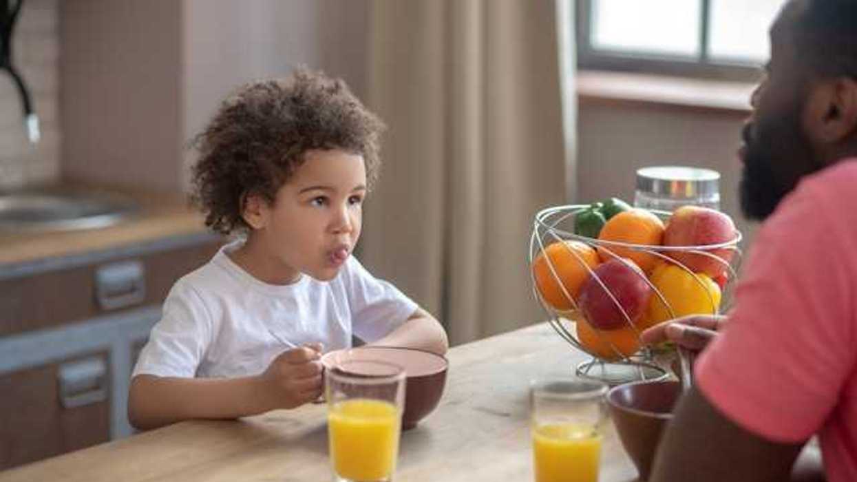 A small child eating breakfast with his dad with fruit and orange juice on the table