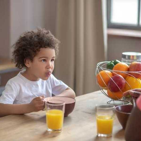 A small child eating breakfast with his dad with fruit and orange juice on the table