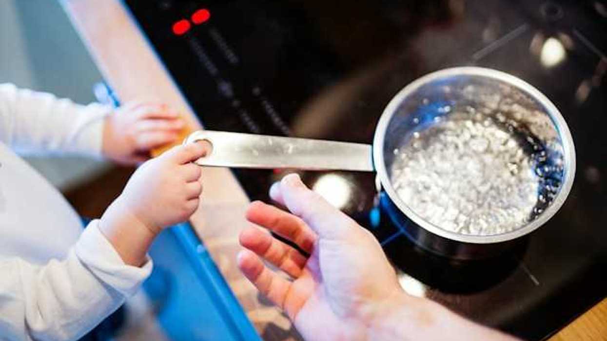 A small child holding the handle of a pot with boiling water
