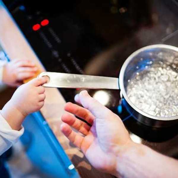 A small child holding the handle of a pot with boiling water