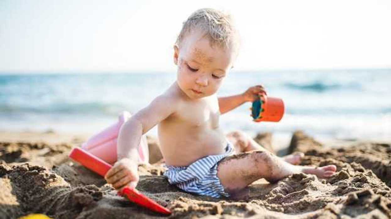 A small child sitting on the sand at a beach playing with plastic toys