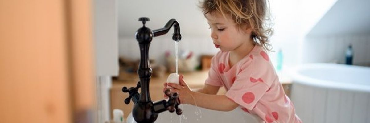 A small child washing her hands at a bathroom sink.