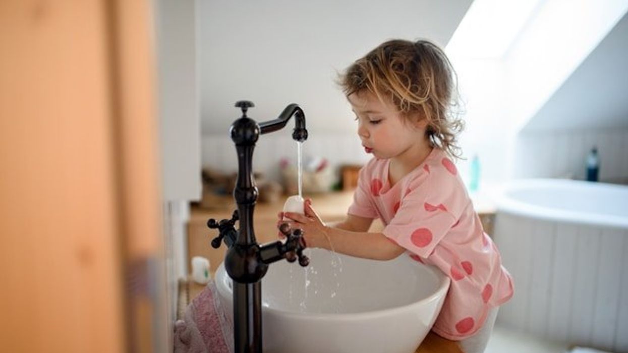 A small child washing her hands at a bathroom sink.