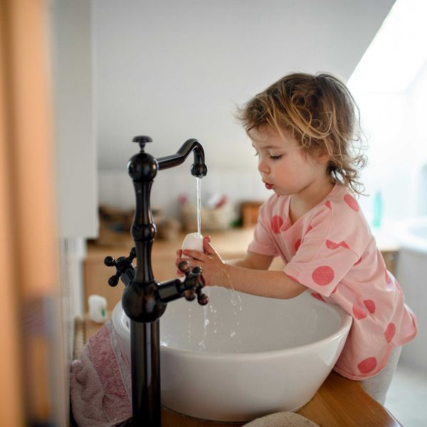 A small child wearing a pink shirt washes her hands with a bar of soap.