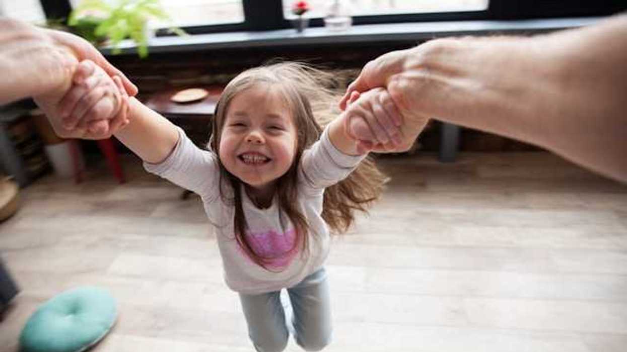 A small girl being twirled in the air by her parent