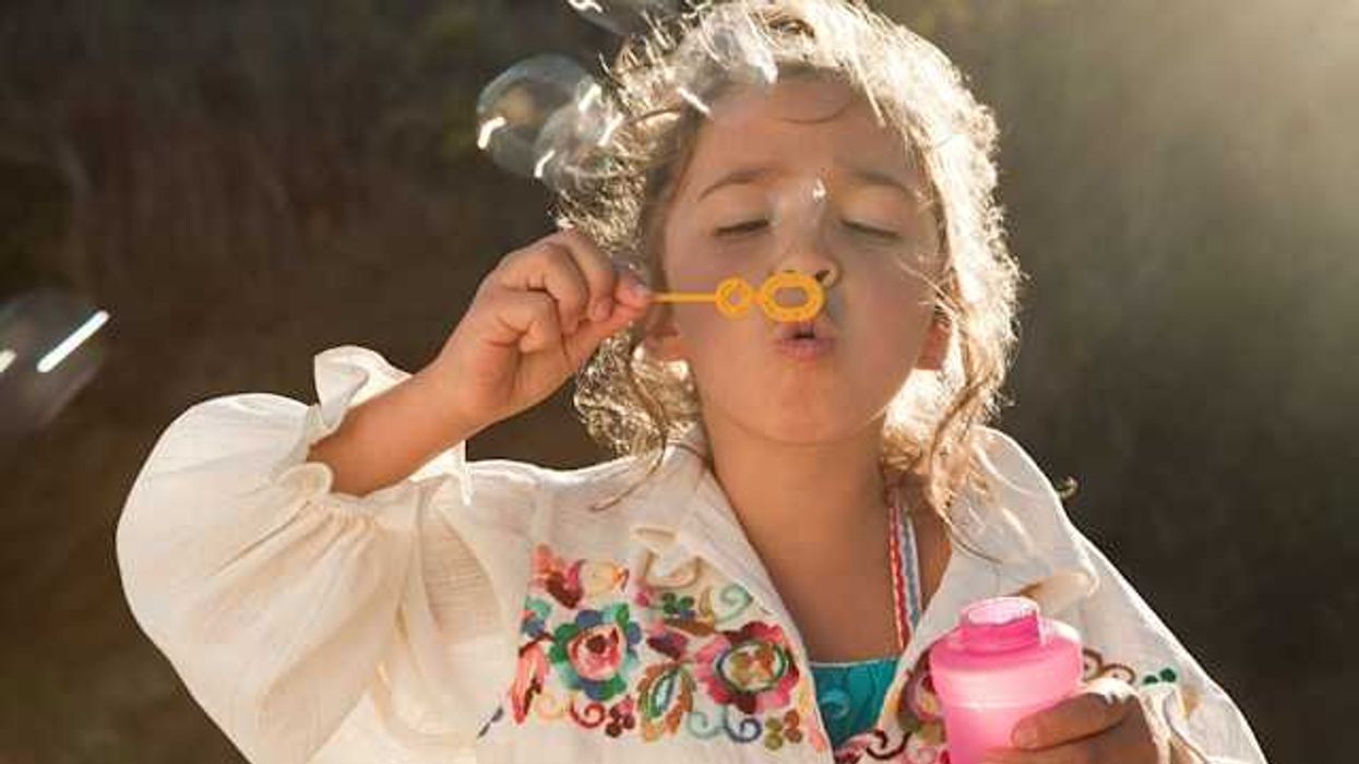 A small girl blowing bubbles from a plastic bubble maker