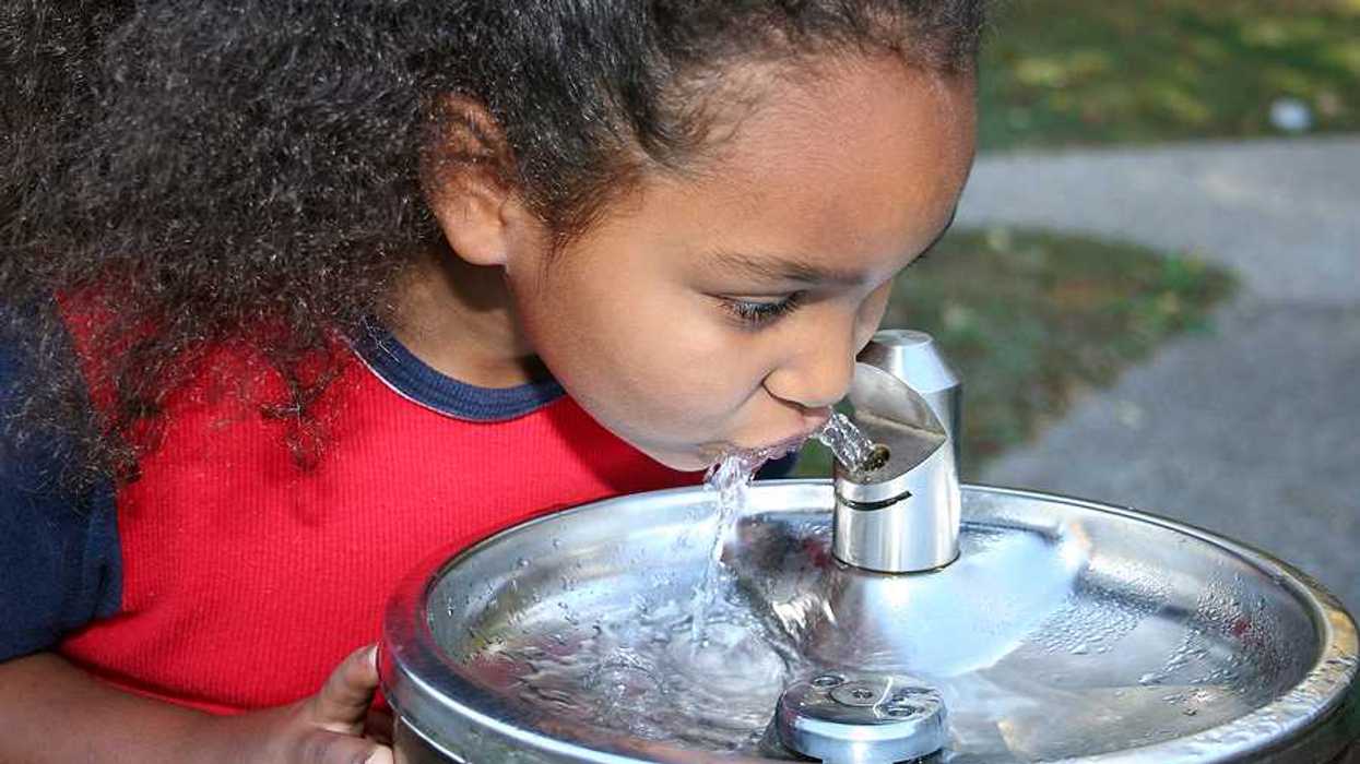 A small girl drinking water out of a silver drinking fountain
