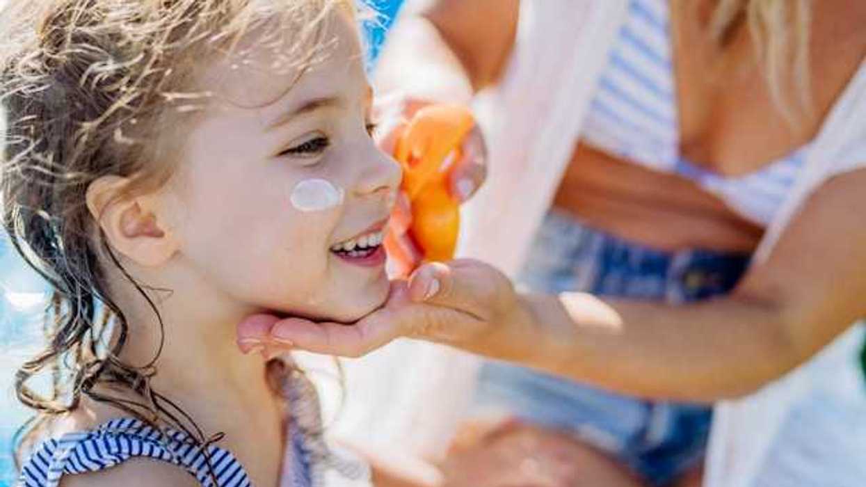 A small girl having sunscreen put on her face