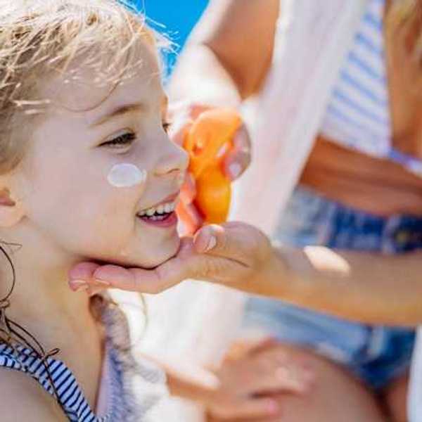 A small girl having sunscreen put on her face