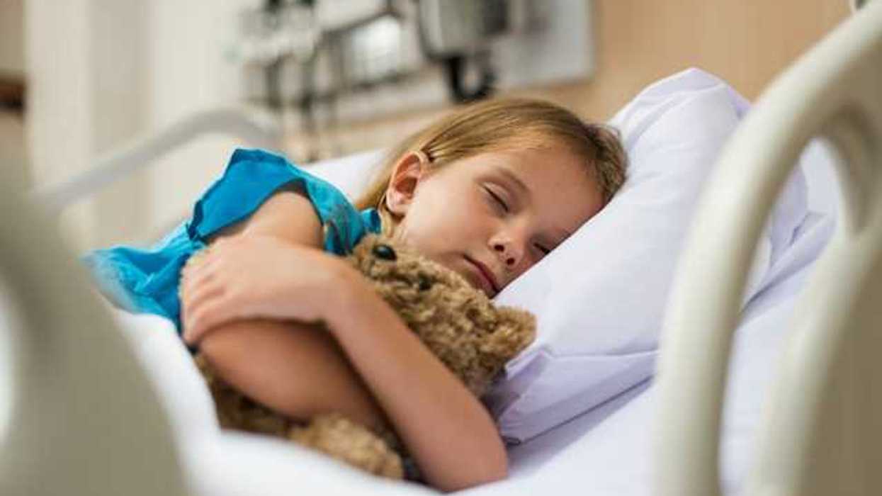 A small girl hugging a teddy bear in a hospital bed