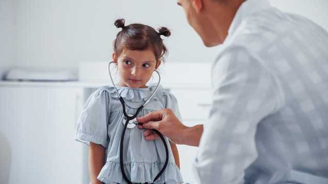 A small girl sitting in front of a doctor holding a stethoscope to her heart