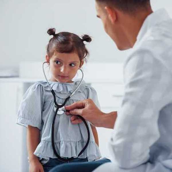 A small girl sitting in front of a doctor holding a stethoscope to her heart