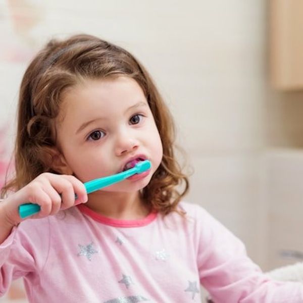 A small girl wearing a pink top brushing her teeth