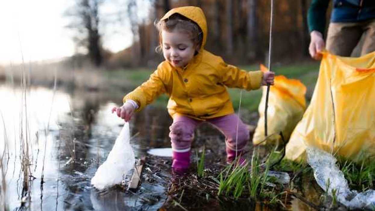 A small girl wearing a yellow rain jacket picking up trash from a creek