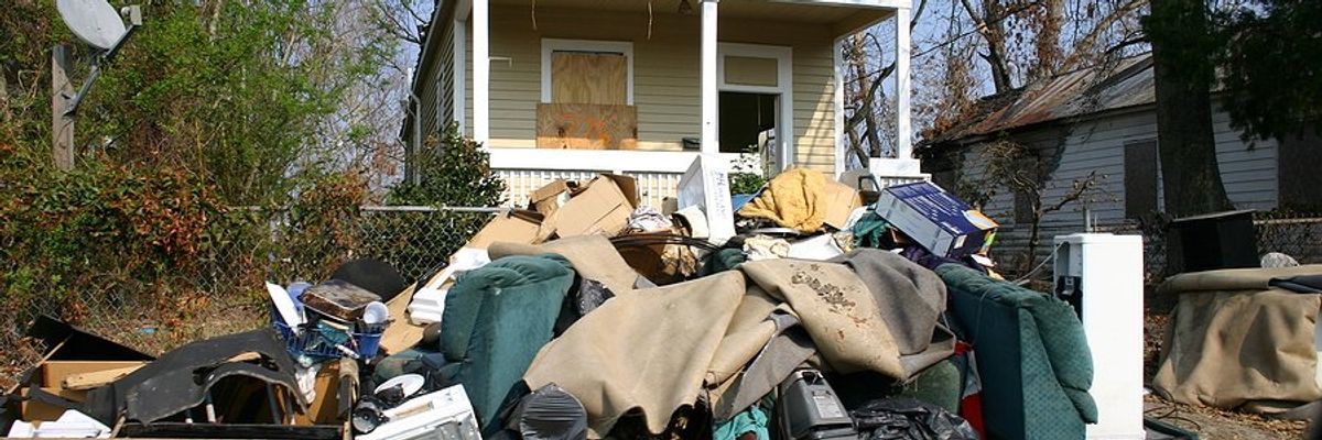 A small home with boarded windows and flood-damaged personal effects piled on the sidewalk
