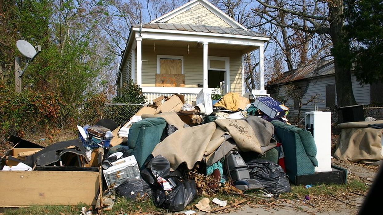 A small home with boarded windows and flood-damaged personal effects piled on the sidewalk