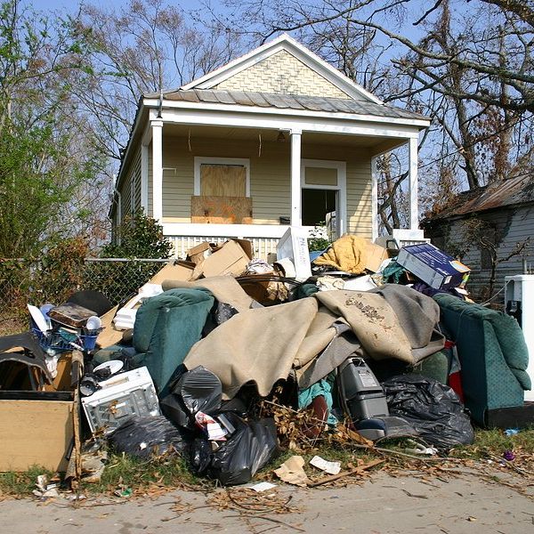 A small home with boarded windows and flood-damaged personal effects piled on the sidewalk