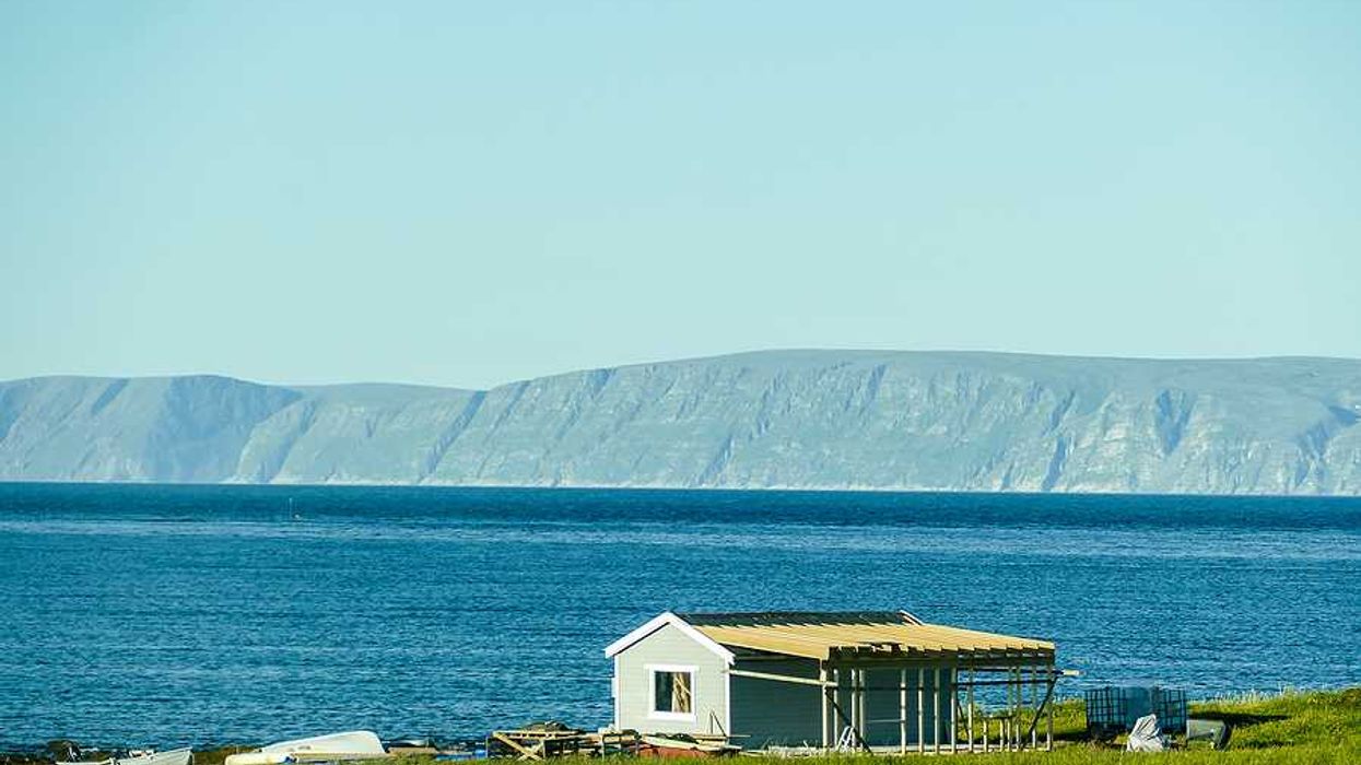 A small house on the edge of the water with mountains in the background