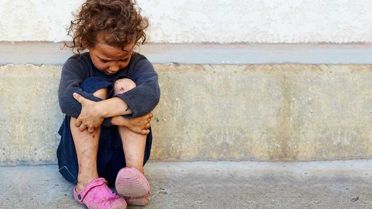 A small impoverished child sitting against a concrete curb