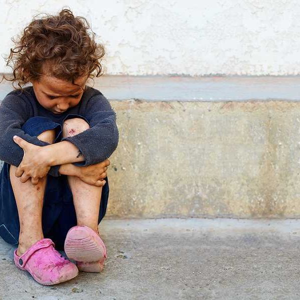 A small impoverished child sitting against a concrete curb