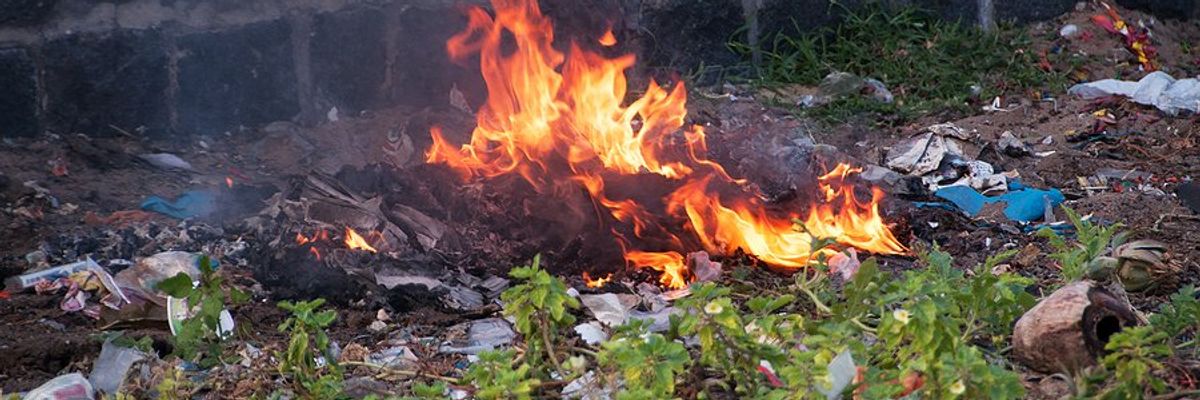 A small pile of burning plastic waste next to a brick wall.